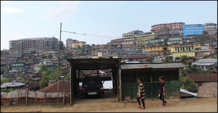 Against the backdrop of high rise buildings, two women are seen walking along a road in a locality of Mon town which has been seeing rapid urbanization of late. (Morung Photo)